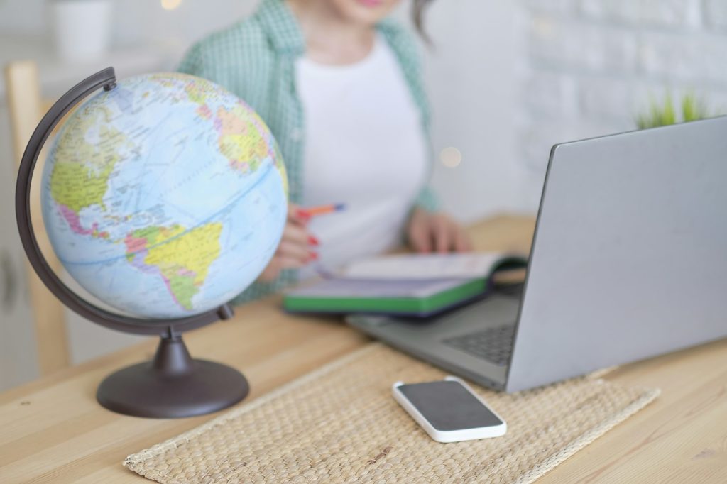 blurred globe in the foreground. in the background a woman works at a laptop