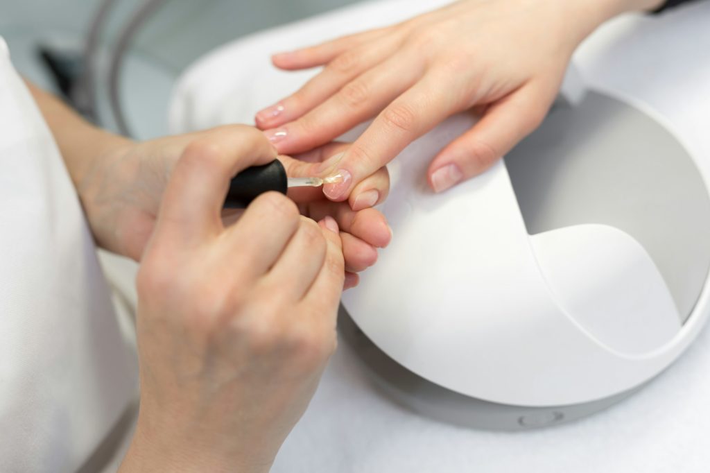 Girl paint nails in the salon of manicure, close-up. Master applies varnish on nails in manicure