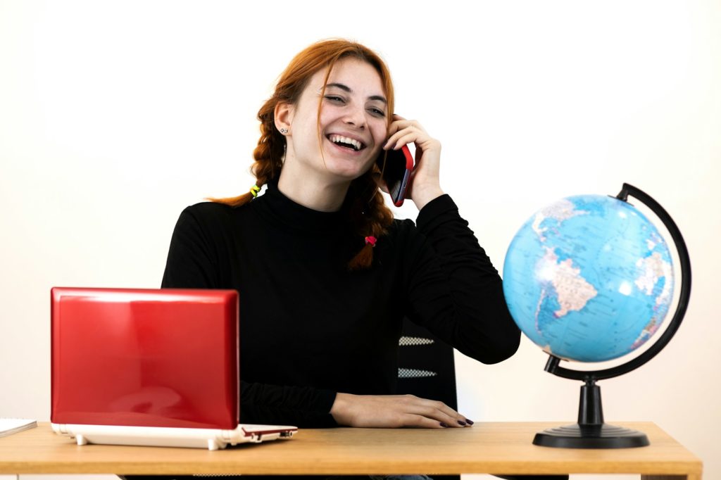Young travel agent woman sitting behind working desk with laptop computer